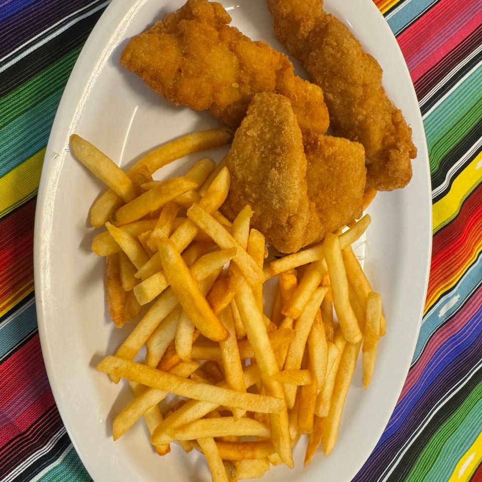 Plate of golden fried fish fillets and French fries on a colorful striped tablecloth.