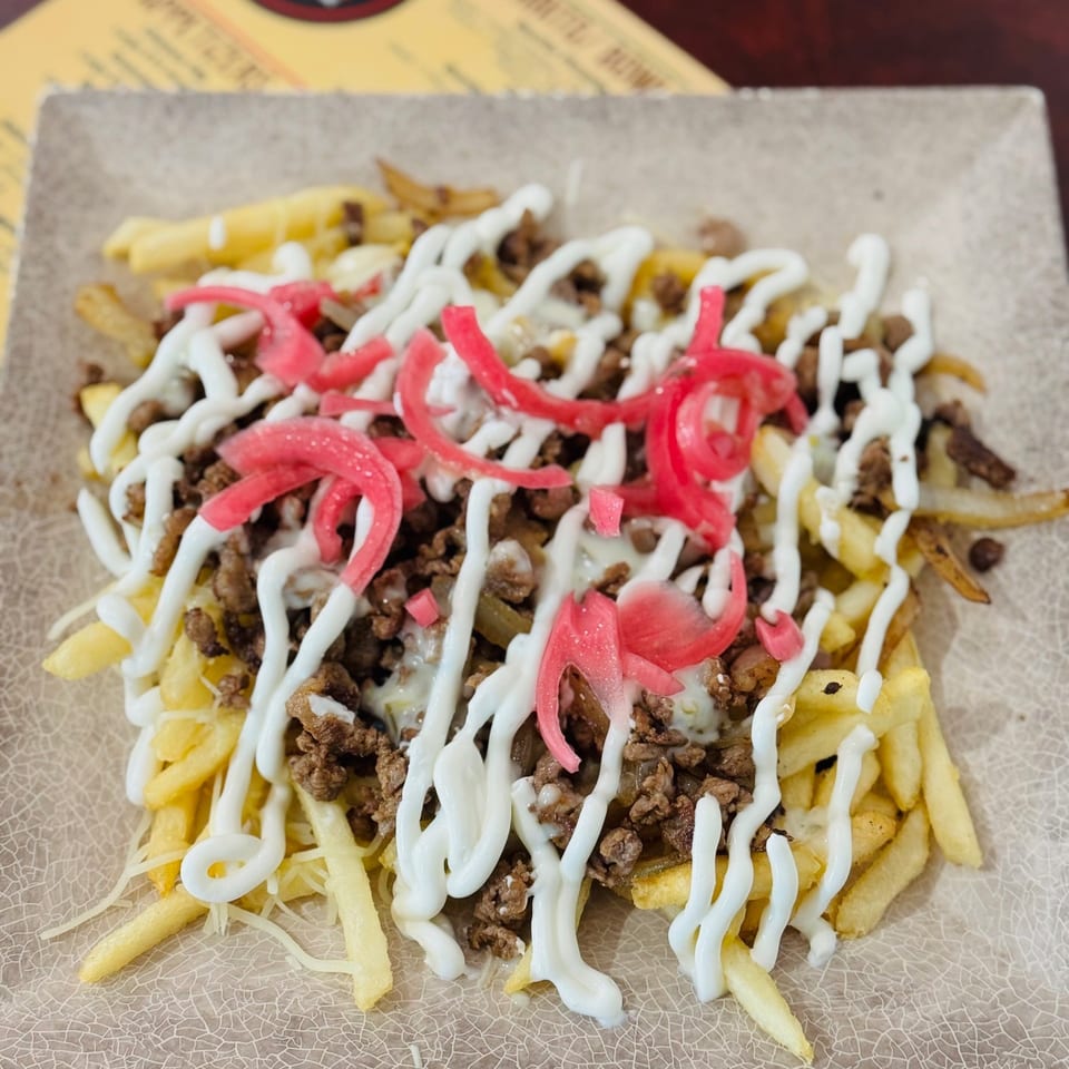 Loaded fries topped with seasoned ground meat, melted cheese, pickled onions, and white sauce on a serving tray.