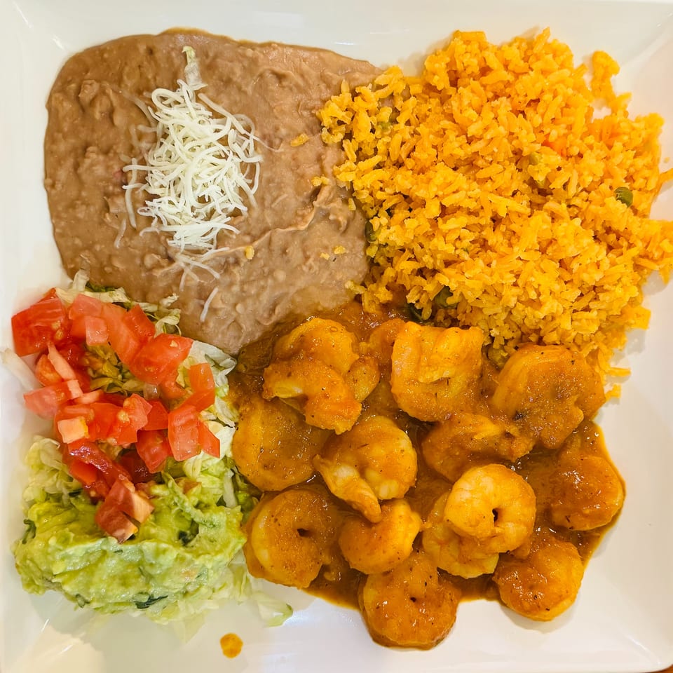 Mexican combination plate with shrimp in sauce, orange rice, refried beans topped with cheese, guacamole, lettuce, and diced tomatoes.
