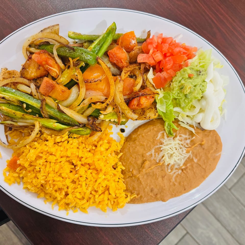 Mexican plate with grilled chicken, peppers, onions, tomatoes, yellow rice, refried beans, guacamole, lettuce, and sour cream.