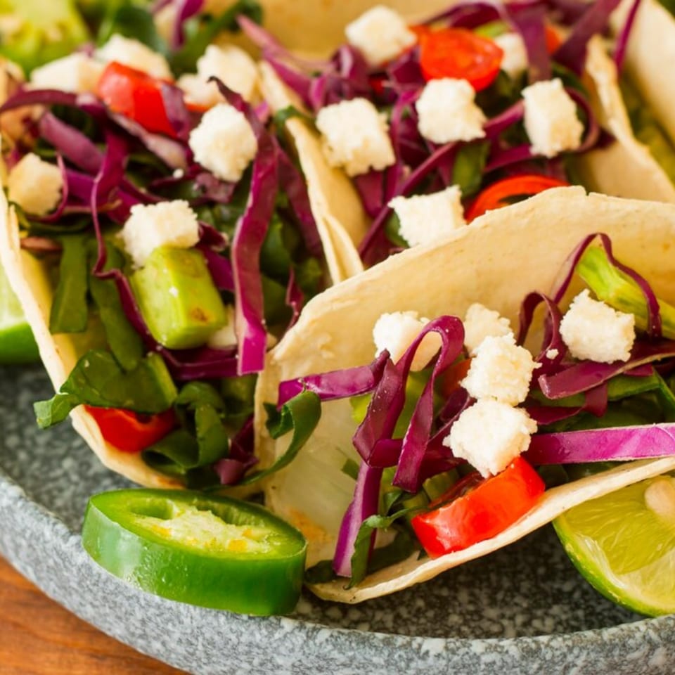 Three Picante Mexican Cuisine tacos filled with red cabbage, tomatoes, and white cheese crumbles.