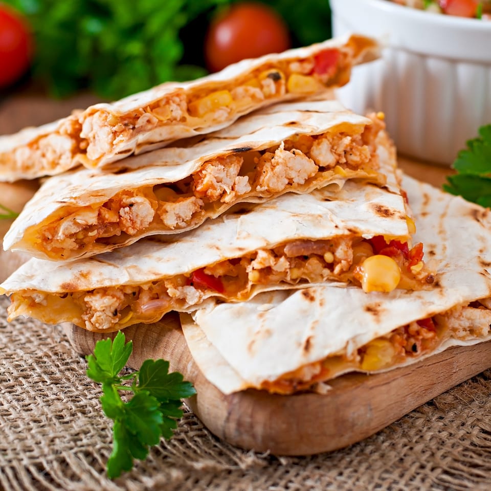 Picante Mexican Cuisine's chicken quesadillas, filled with cheese, corn, and peppers, on a wooden board.